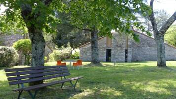 An outdoor seating area with a bench and chairs, a stone building, and a tree providing shade.