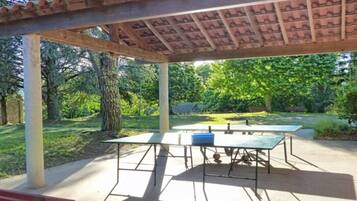 Een terras buiten met een pergola, twee tafels en een bank.