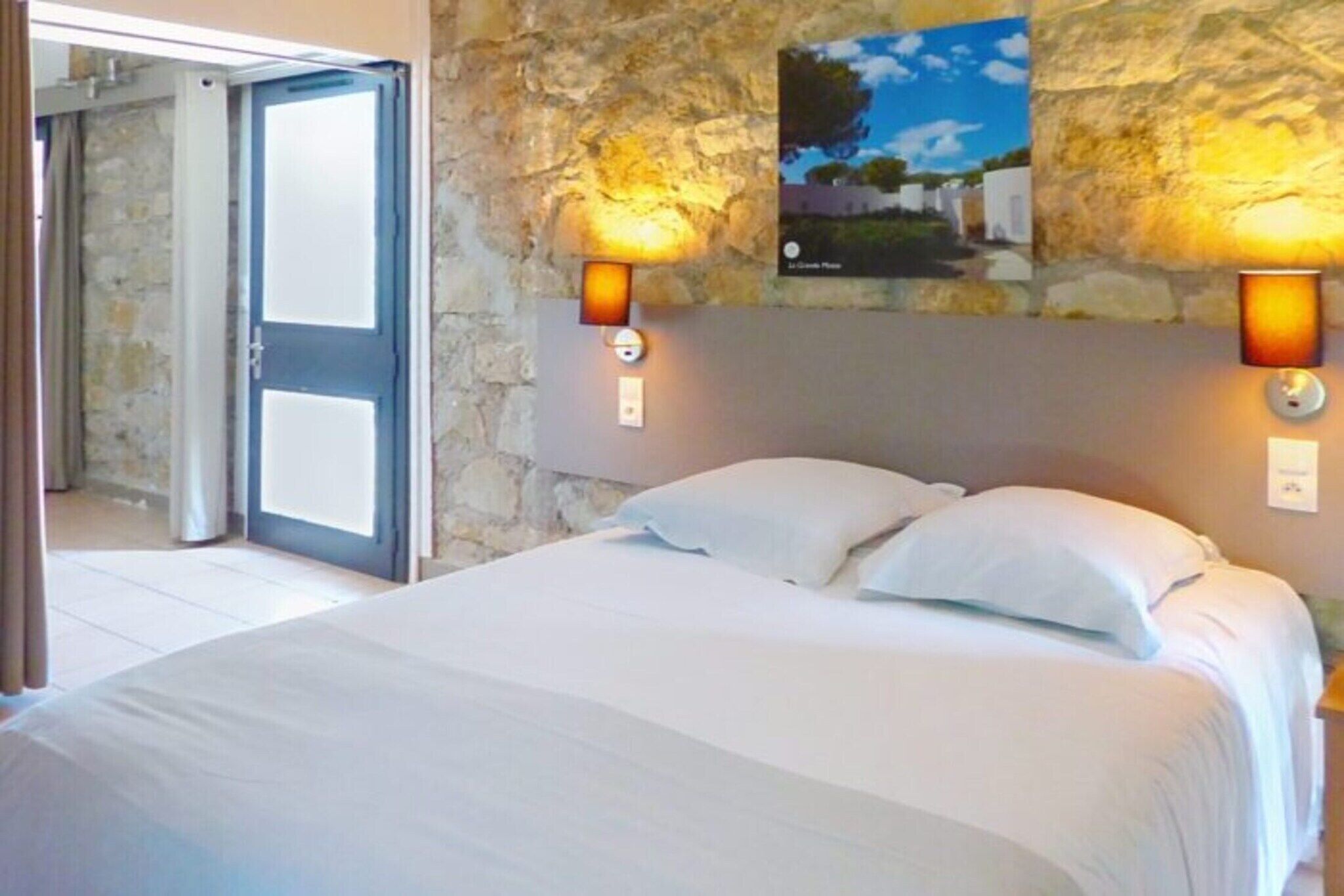 A hotel room with a bed, a stone wall, and two wall-mounted lamps.