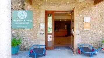A stone building entrance with a sign for 'Terres de France Domaine des Vans' and two blue wheelchairs outside.