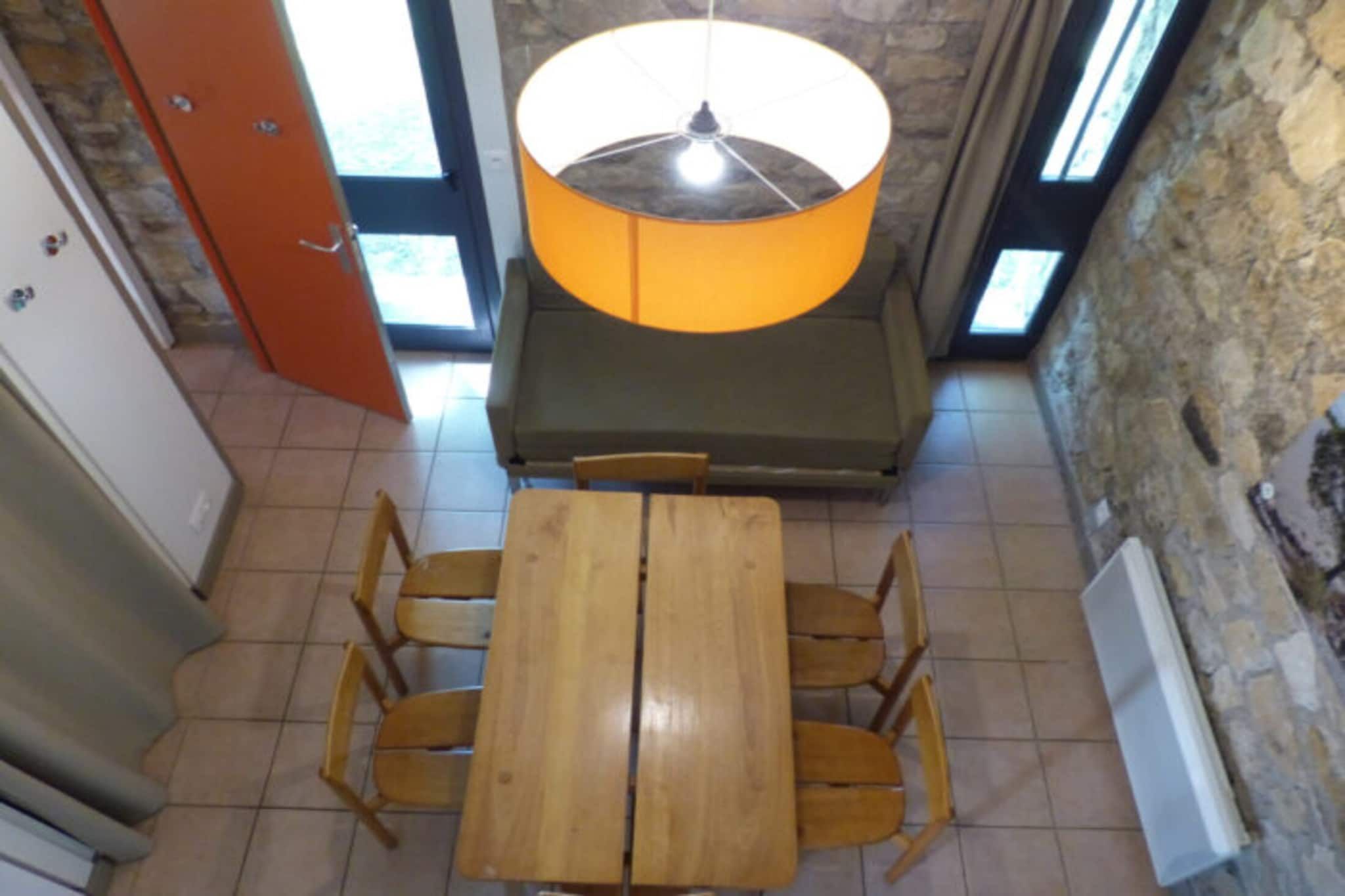 A room with a wooden table and chairs, a stone wall, and a large window.
