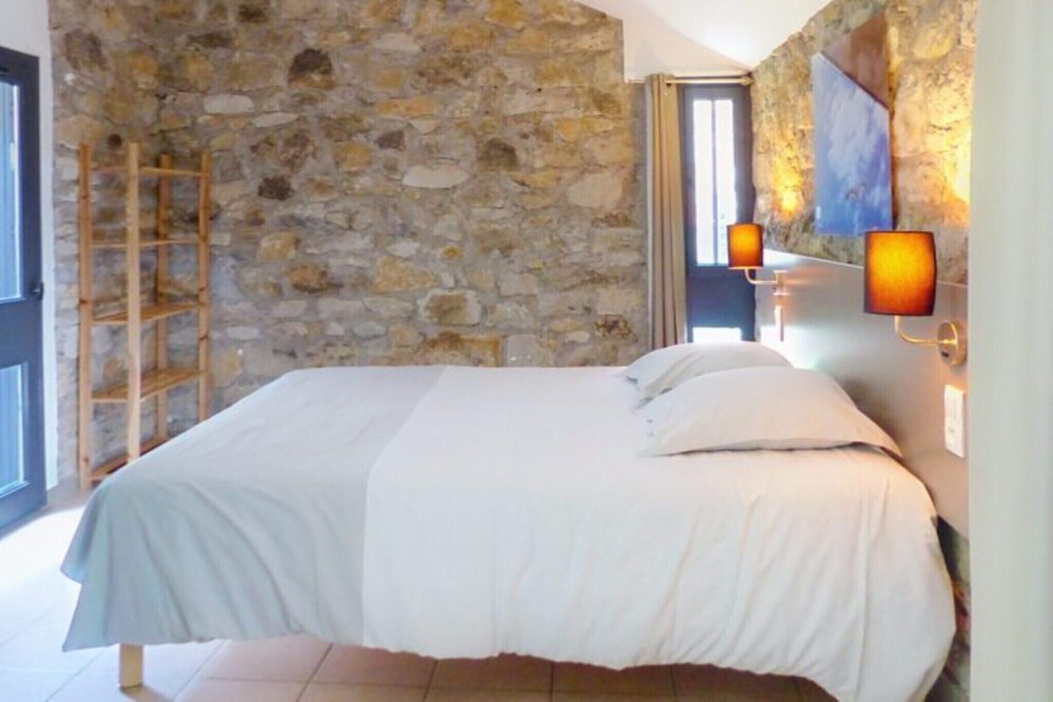 A bedroom with a stone wall, a bed with white bedding, and two wall-mounted lamps.