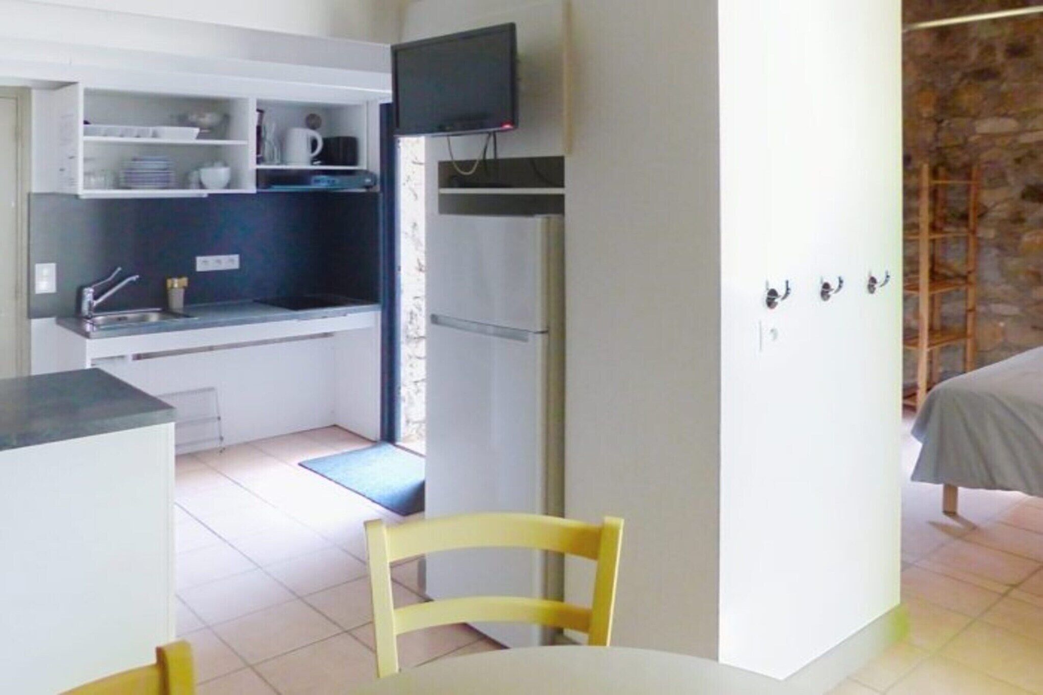 Una cocina compacta con refrigerador, microondas y lavamanos. Hay un pequeño comedor con una silla y una mesa.