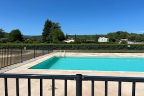 A rectangular swimming pool with a black metal fence, surrounded by greenery and houses in the background.