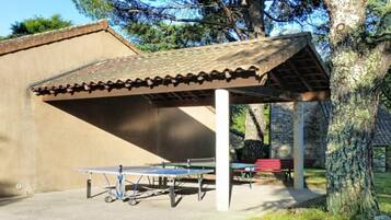A covered outdoor area with a ping pong table and benches.