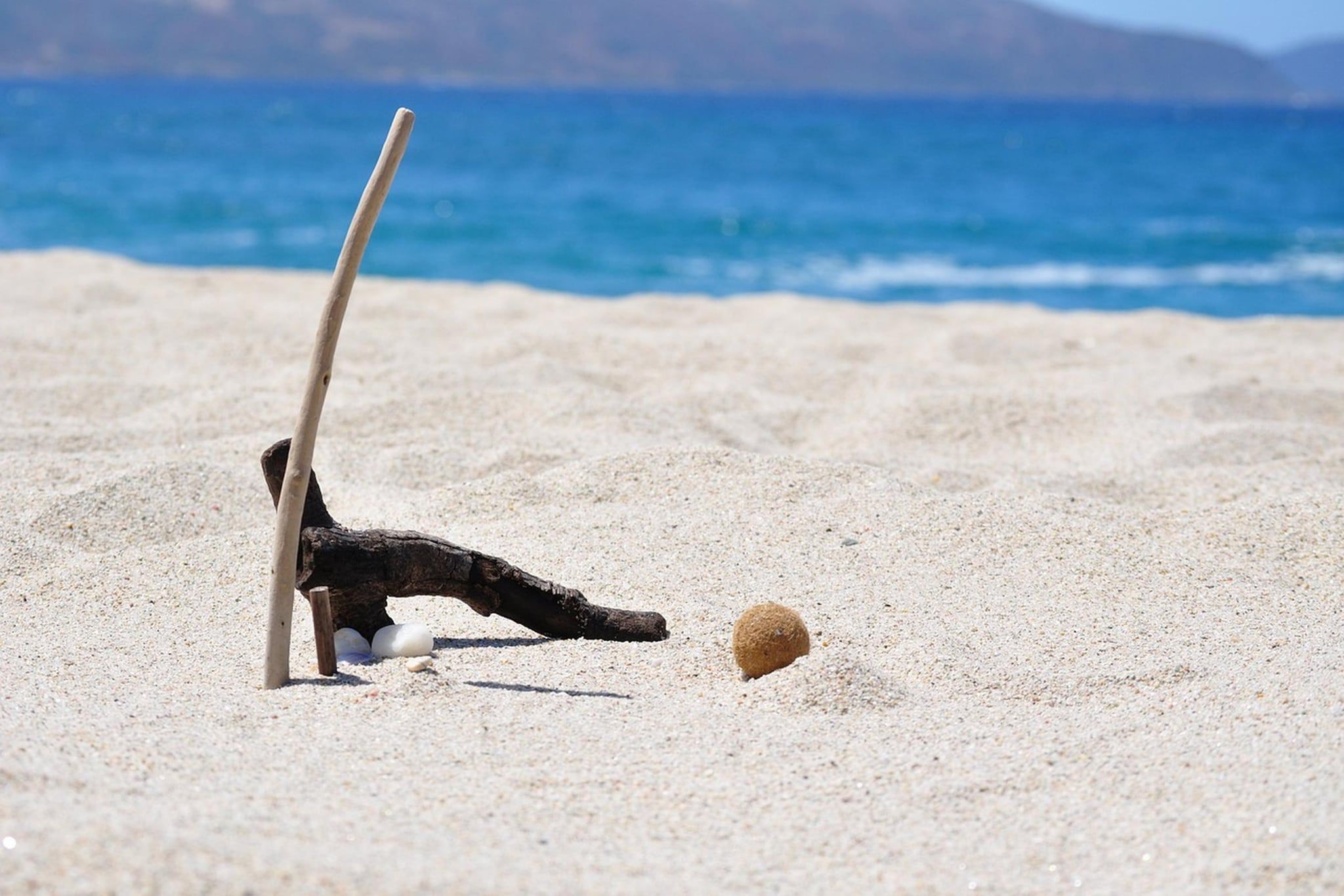 A beach scene with a wooden structure, a stick, and a ball on the sand.