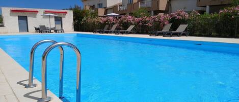 A swimming pool with lounge chairs and a building in the background.