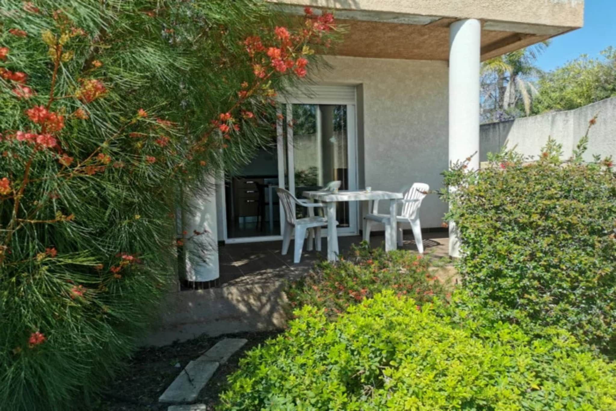 A patio with a table and chairs, surrounded by greenery and a building with a glass door.