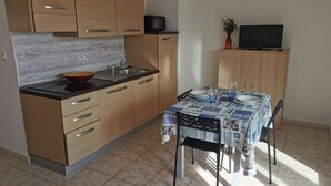Een kleine keuken met houten kastjes, een magnetron, een eettafel met stoelen en een televisie op een standaard.