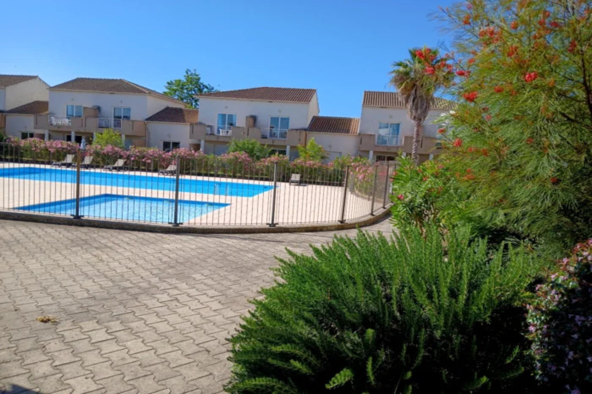 A swimming pool with a white fence, surrounded by greenery and residential buildings.