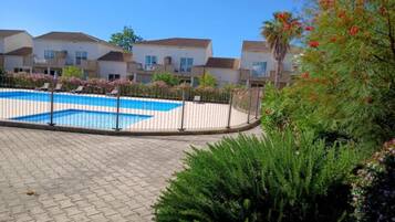 A swimming pool with a white fence, surrounded by greenery and residential buildings.