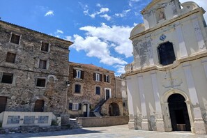 A historic building with a clock tower, stone walls, and a staircase leading to an entrance. - Family Duplex with Terrace in Corsica (Linguizzetta)
