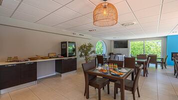 A modern kitchen with dark cabinetry, a dining area with wicker chairs, and a large window offering a view of greenery.