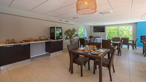 Una cocina moderna con armarios oscuros, un comedor con sillas de mimbre y un ventanal que ofrece vistas al verdor.