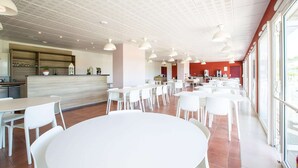A spacious dining area with white tables and chairs, a kitchen area with a counter, and large windows providing natural light. - Couple Stay Near Mont-Saint-Michel (Roz-sur-Couesnon)