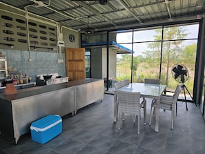 A modern kitchen with a large island, a dining area with wicker chairs, and a view of greenery outside.