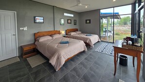 Habitación de hotel con dos camas, ventilador de techo, ventana grande y vista al exterior.