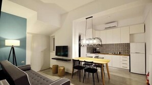 A modern living room with a sofa, a dining table with chairs, a TV, and a kitchen area with cabinets and a refrigerator. - Casa al Porto (Zakinthos)