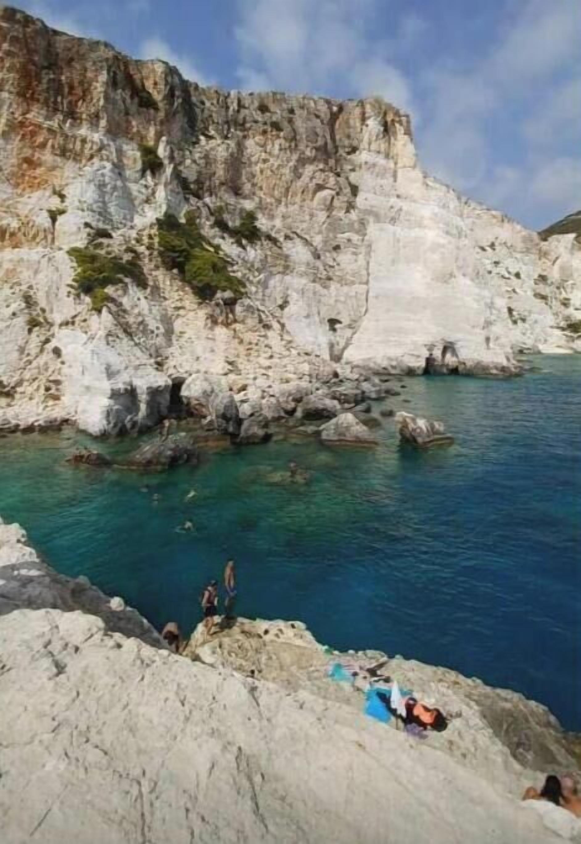 Une falaise côtière surplombant une eau d’un bleu limpide, un paysage rocheux et des personnes pratiquant diverses activités de plein air.