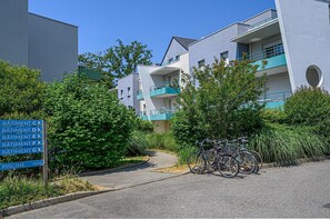 Un immeuble résidentiel doté de nombreux balcons, d’un panneau indiquant les directions vers les différents appartements et d’une piscine, ainsi que de vélos garés devant.