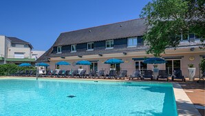 A swimming pool with lounge chairs and umbrellas, a building with a sloped roof, and a clear blue sky. - Cozy Apartment Stay Near Vannes (Plescop)