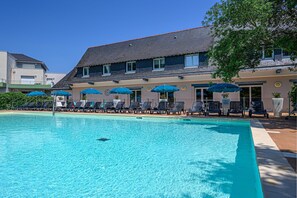 Een zwembad met ligbedden en parasols, een gebouw met schuin dak en een helderblauwe lucht.