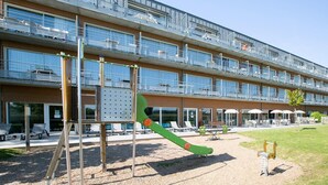 Un parque infantil con columpios y un tobogán frente a un edificio moderno con varios balcones.