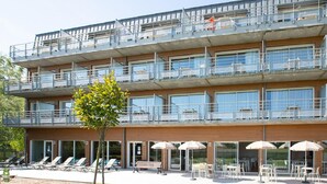 Un hotel de diversos pisos amb terrassa exterior, piscina i un arbre al primer pla.