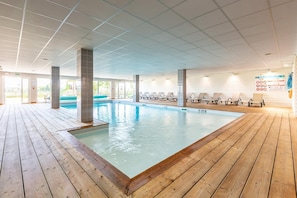 Ein Innenpool mit Holzterrasse, Liegestühlen und einer gefliesten Decke.