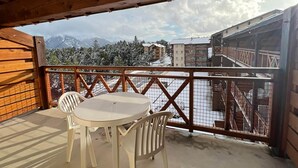 Ein Holzbalkon mit Tisch und Stühlen, mit Blick auf eine verschneite Berglandschaft und Gebäude.