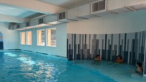 Ein Hallenbad mit klarem Wasser, einer mit vertikalen Mustern gefliesten Wand und einer Decke mit Lüftungsöffnungen.