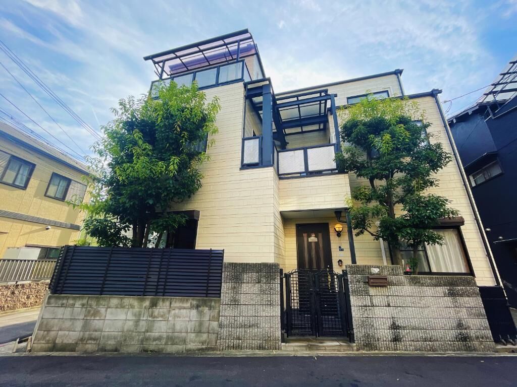 A modern two-story building with a flat roof, large windows, and a black gate.