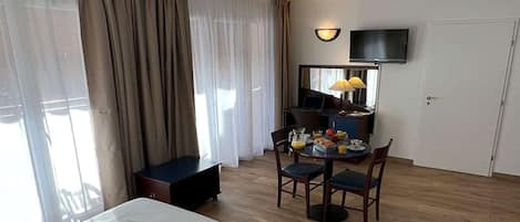 A hotel room with a bed, a desk with a chair, a television, and a dining table with chairs.