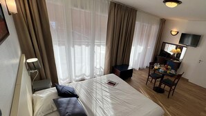 Een hotelkamer met een bed, een bureau met stoel, een televisie en een raam met gordijnen.