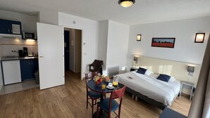 Hotelkamer met een bed, nachtkastje, wandlamp en een zithoek met tafel en stoelen.