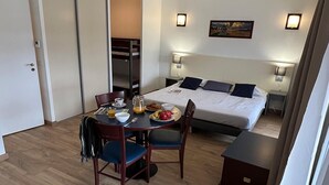 A hotel room with a bed, bedside tables, a dining table with chairs, a small kitchen area, and a bunk bed in the background. - 4-persons studio with balcony (BOLQUERE)