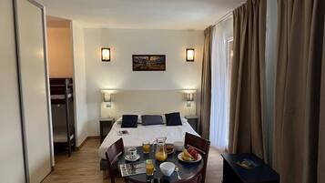 Une chambre d’hôtel avec un lit, des lampes de chevet, une table avec le petit-déjeuner et un tableau au mur.