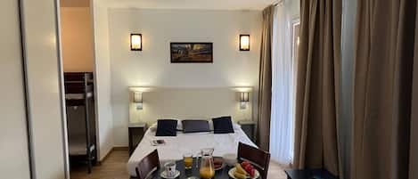A hotel room with a bed, bedside lamps, a table with breakfast, and a painting on the wall.