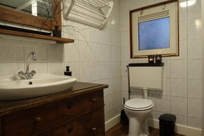 Ein Badezimmer mit Waschbecken, Holzschrank, Toilette und einem Spiegel mit Fenster darüber, das einen blauen Schimmer hat.