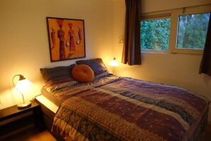 Ein Schlafzimmer mit Bett, Nachttisch, Lampe, einem Gemälde und einem Fenster.