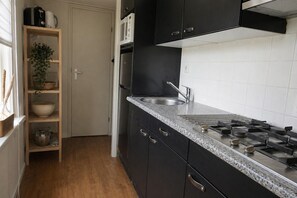 A kitchen with a granite countertop, stainless steel appliances, and a wooden shelf unit.