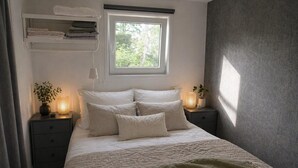 A bedroom with a bed, bedside tables, a window, and a shelf with folded towels. - Vechtdal Chalet de Berk (Rheezerveen)