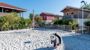 Een zandig gebied met een panda standbeeld, houten hekken en gebouwen met rode daken.