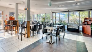 Een moderne eethoek met tafels, stoelen, een bank en een boekenkast.