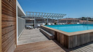Eine Holzterrasse mit Pool, Liegestühlen und einer Pergola.