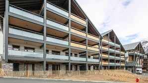 A multi-story building with balconies, stone facade, and a mountainous backdrop. - 2-Person Studio near Ski Lifts (VAUJANY (ISERE))