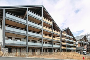 A multi-story building with balconies, stone facade, and a mountainous backdrop. - 2-Person Studio near Ski Lifts (VAUJANY (ISERE))