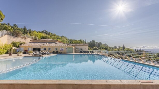 A swimming pool with a sunlit sky, a building with a tiled roof, and a view of the sea. - Apartment for 4 with Private Terrace (CALLIAN (VAR))