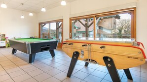 Een poolzaal met twee pooltafels, houten kasten en grote ramen.