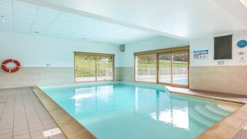 An indoor swimming pool with clear glass windows, a tiled floor, and a life preserver on the wall.